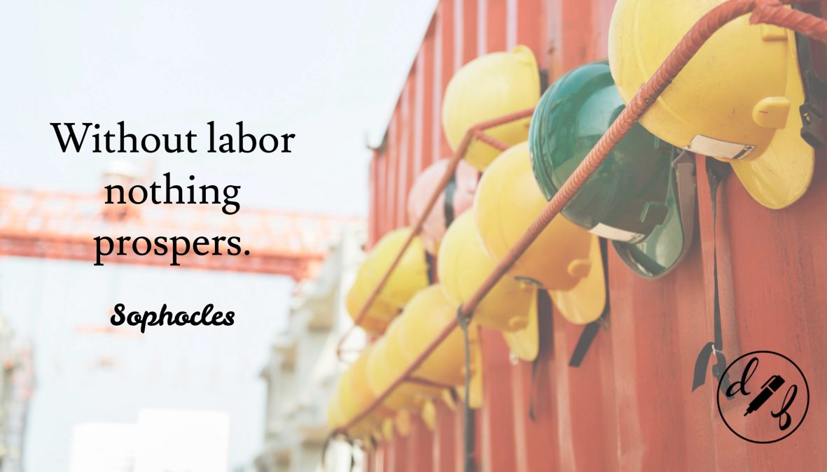 A row of hard hats hanging on a red wall outside with a quote by Sophocles