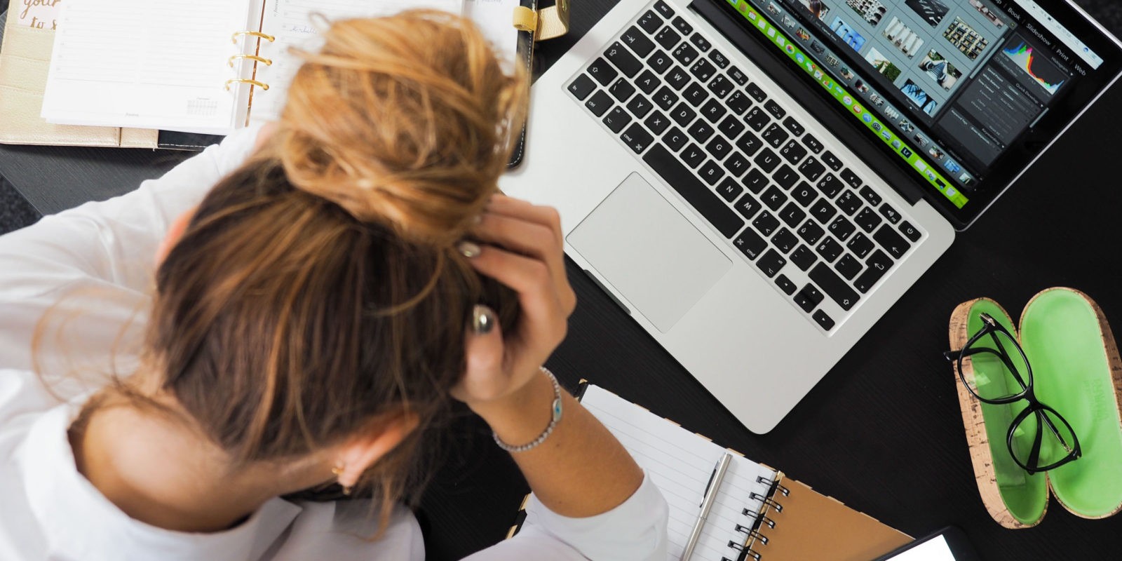 A woman with a bun sits with her hand at her head while looking at her laptop computer
